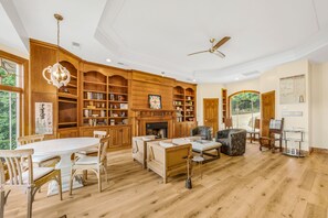 A spacious living room with a fireplace, wooden bookshelves, a dining area, and a ceiling fan.