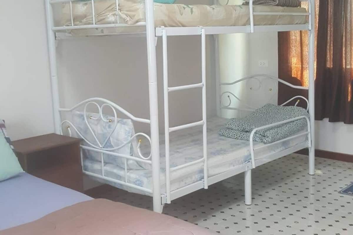 Une chambre avec un lit superposé, un lit simple, une petite table et un sol à motifs.