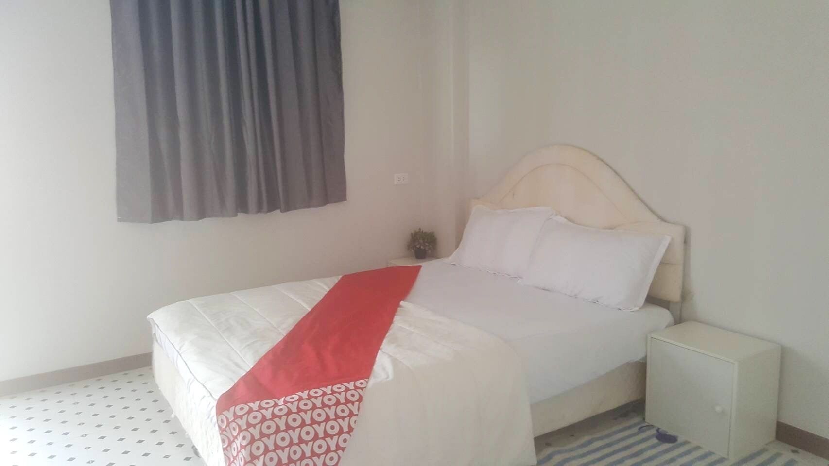 A single bed with a white and red bedspread, a bedside table, and a small cabinet.