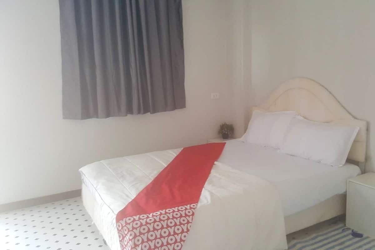 Un lit simple avec une couvre-lit blanche et rouge, une table de chevet et une petite armoire.