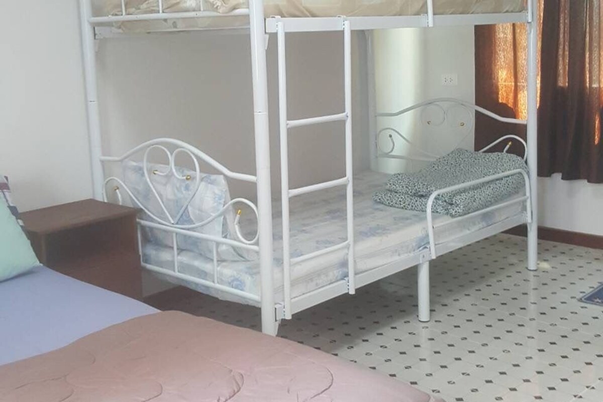 Une chambre avec un lit superposé, un lit simple, une petite table et un sol à motifs.