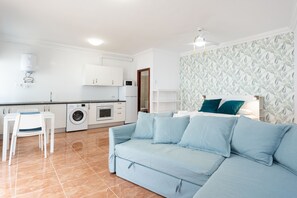 Una sala de estar moderna con un sofá, una mesa de comedor con sillas, una lavadora y una zona de cocina.