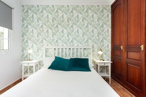 Un dormitorio con cama, dos mesitas de noche con lámparas, un armario de madera y un papel tapiz estampado.