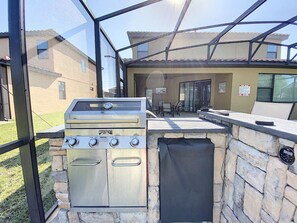 Une cuisine extérieure dotée d’un barbecue en acier inoxydable, de murs en pierre et d’une structure en verre.