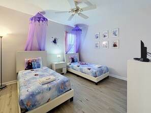 A bedroom with two beds, a ceiling fan, bedside lamps, a desk, and a TV.