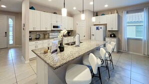 A modern kitchen with white cabinets, granite countertops, and pendant lighting. - Magical Express: Private Pool & 24/7 Support (Davenport)