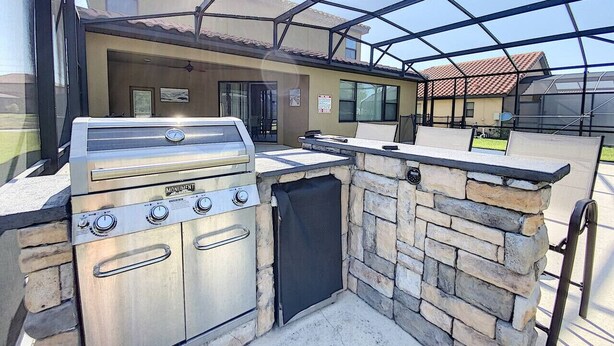 An outdoor kitchen with a stainless steel grill, stone walls, and a glass enclosure. - Magical Express: Private Pool & 24/7 Support (Davenport)