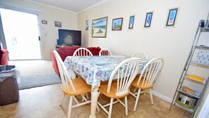 Un comedor con una mesa lista para cuatro personas, rodeada de sillas blancas con asientos de madera.