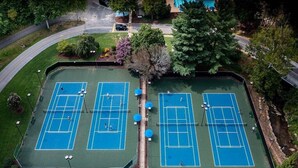 Une vue aérienne d’un complexe de courts de tennis, comprenant plusieurs terrains, entouré de verdure et bordé par une route.