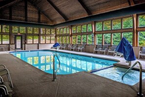 An indoor swimming pool with clear windows, a covered seating area, and a wooden ceiling. - Bent Creek 28 at Rumbling Bald (Lake Lure)
