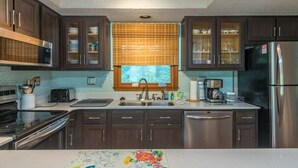 Une cuisine moderne avec des meubles en bois foncé, des appareils électroménagers en acier inoxydable et une fenêtre équipée de stores.