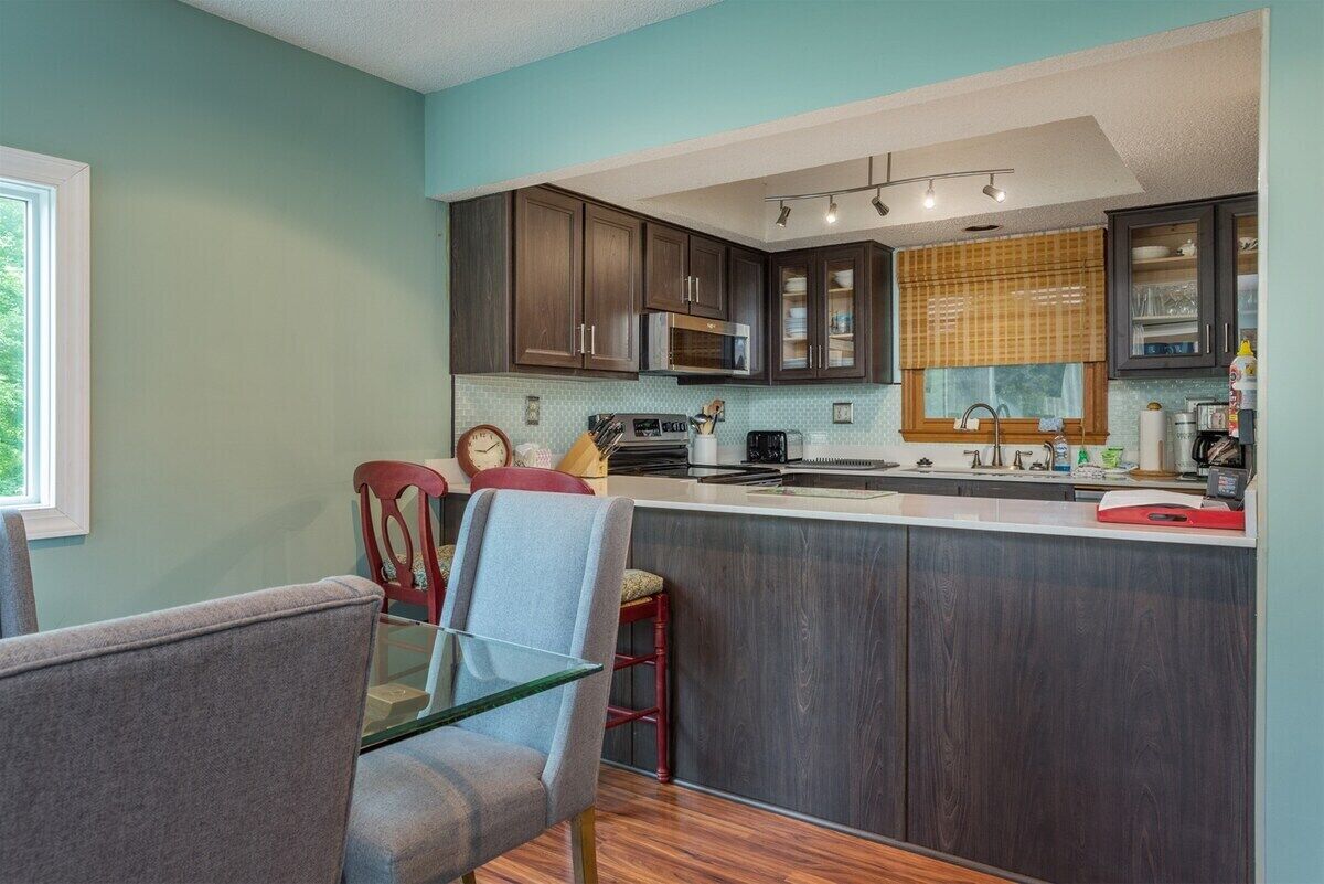 A kitchen with dark wooden cabinets, a stainless steel microwave, and a window with blinds.