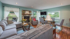 Un salon comprenant un canapé, des fauteuils, une table basse, une cheminée, un téléviseur et un coin repas avec des chaises et une table.