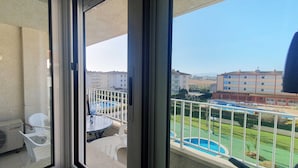 Ein Balkon mit Glastür, weißen Stühlen, einem kleinen Tisch und Blick auf den Pool.