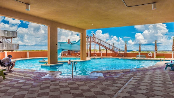 A swimming pool with a water slide, palm trees, and a clear sky.