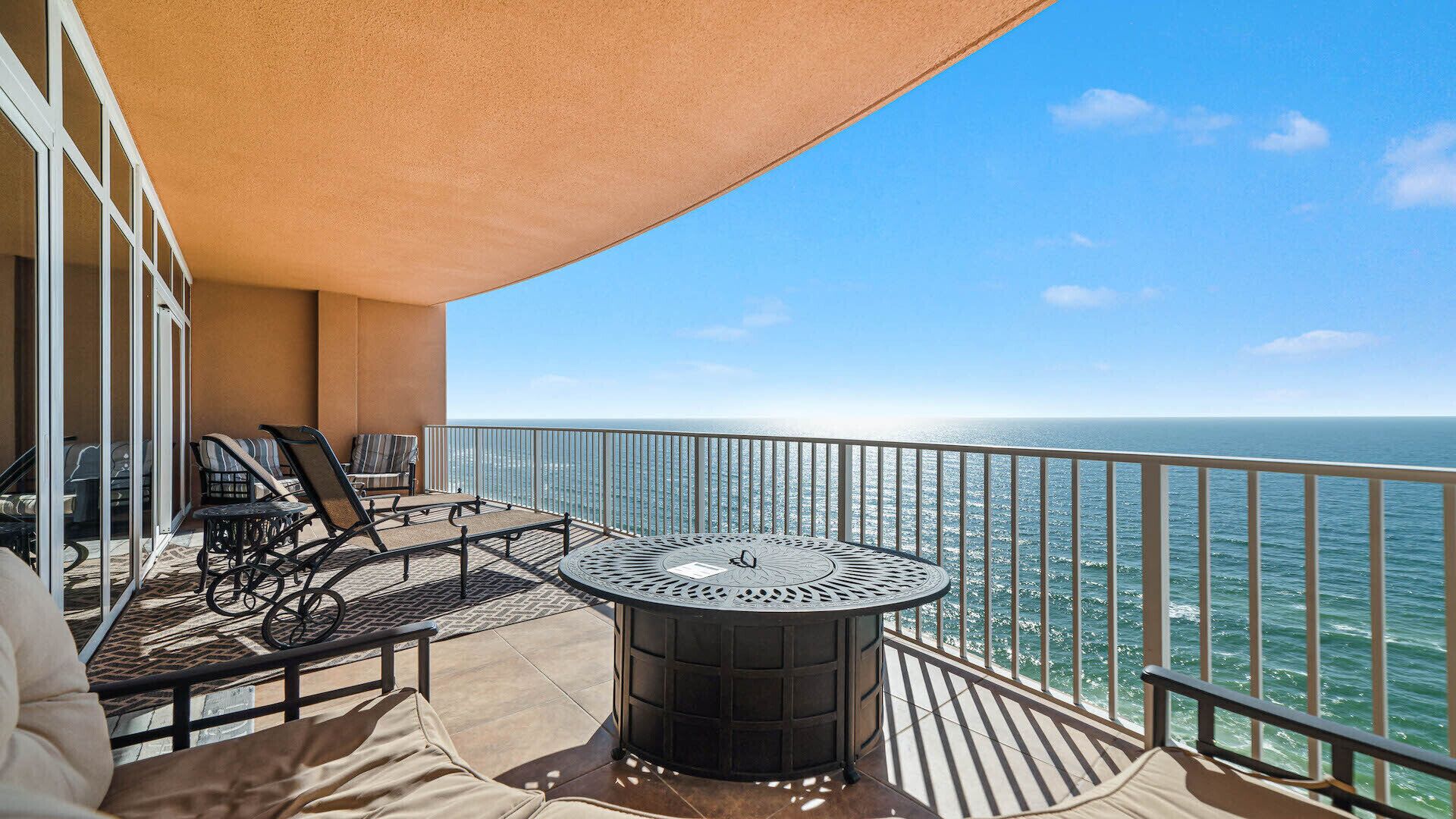 A balcony with a round table and chairs, overlooking the ocean.