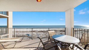 A balcony with a table and chairs, overlooking a beach with a clear view of the ocean.