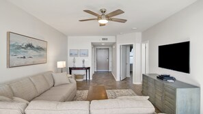 A living room with a sofa, a coffee table, a TV, and a ceiling fan.