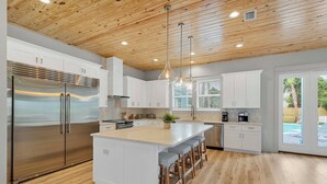 A modern kitchen with wooden ceiling, stainless steel appliances, and a central island with bar stools. - Poseidon's Palace | Private Pool/Spa | 6-Seater Golf Cart | Game Room (Destin)