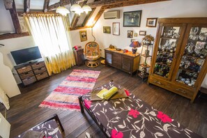 A cozy room with a bed, a chair, a TV, a cabinet with glass doors, and a wooden ceiling.