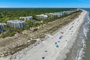 Een kusthotel met meerdere gebouwen, een zandstrand en parasols.