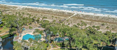 A resort with a swimming pool, beachfront access, and lush greenery.