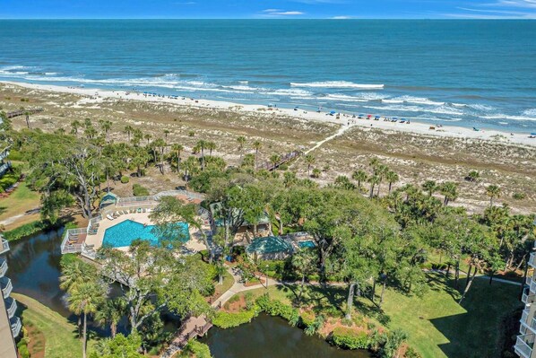 Un resort con piscina, acceso a la playa y abundante vegetación.