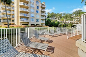 A deck with sun loungers and a view of a multi-story building with balconies. - Oceanfront Villa Direct Beach Access (Hilton Head Island)