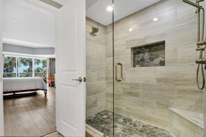 Habitación de hotel con una cama, un vidrio corredizo que da a un balcón y una zona de ducha con un resplandor de mosaico de piedra.