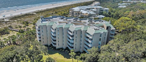 A multi-story hotel with a central courtyard, surrounded by dense greenery and a view of the beach.