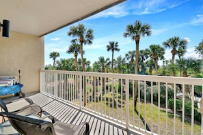 Een balkon met uitzicht op palmbomen, een witte reling en een kar met bagage.