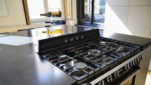 A kitchen with a black Smeg gas stove, a window with blinds, and a bottle of alcohol on the counter. - Spacious apartment in old Lyon historical location (Lyon)