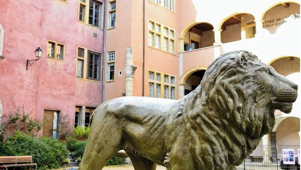 A lion statue in an outdoor courtyard with a pink building in the background. - Spacious apartment in old Lyon historical location (Lyon)