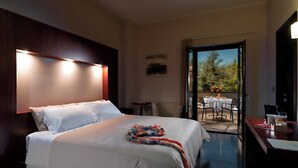 Habitación de hotel con cama, una pequeña mesa con silla, y balcón con mesa y sillas.