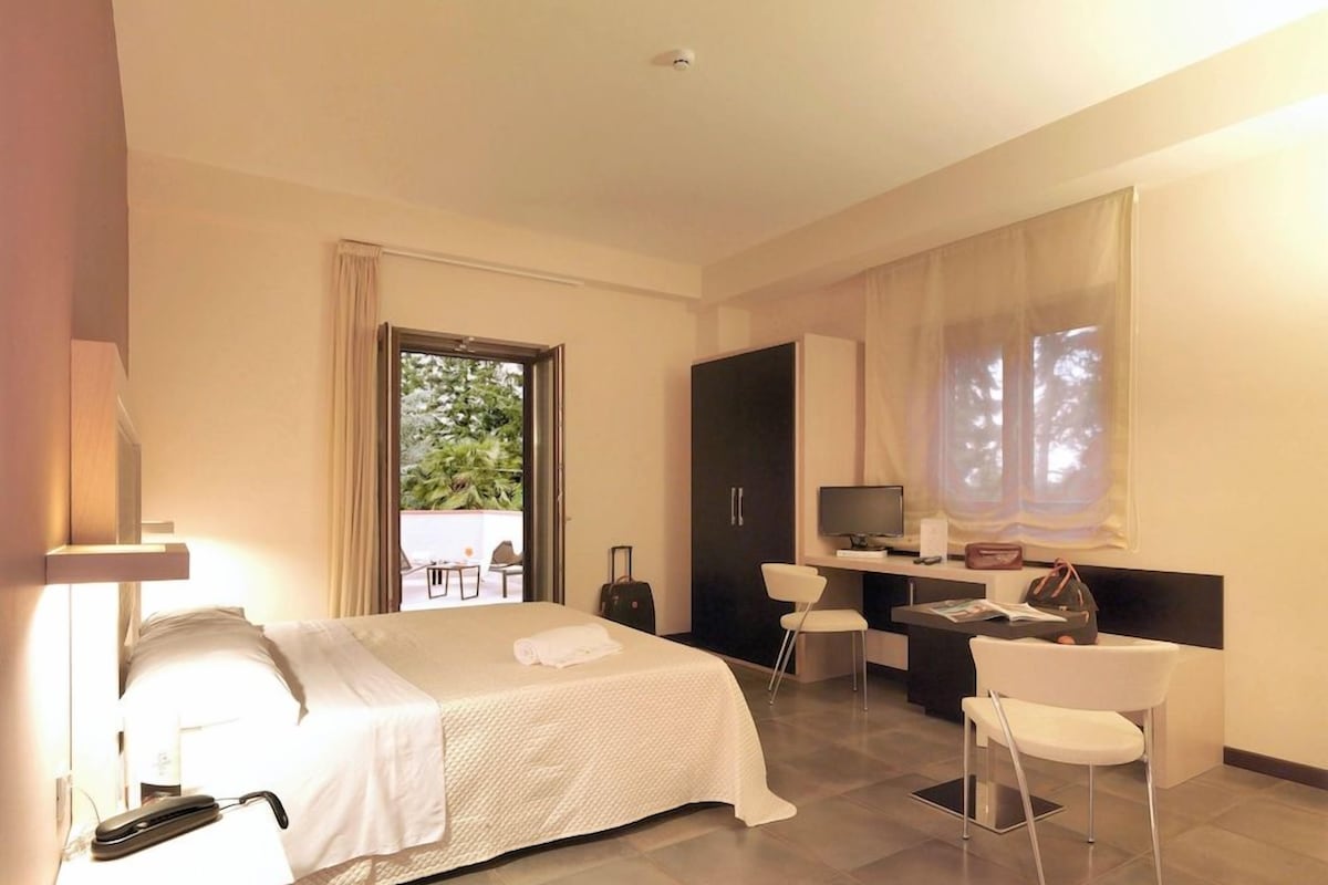 Une chambre d’hôtel avec un lit, un bureau, une chaise, une télévision et une fenêtre avec des rideaux.