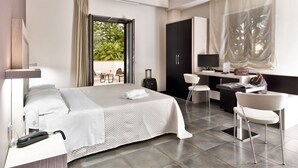 Habitación de hotel con cama, escritorio, silla y vista a zonas verdes.