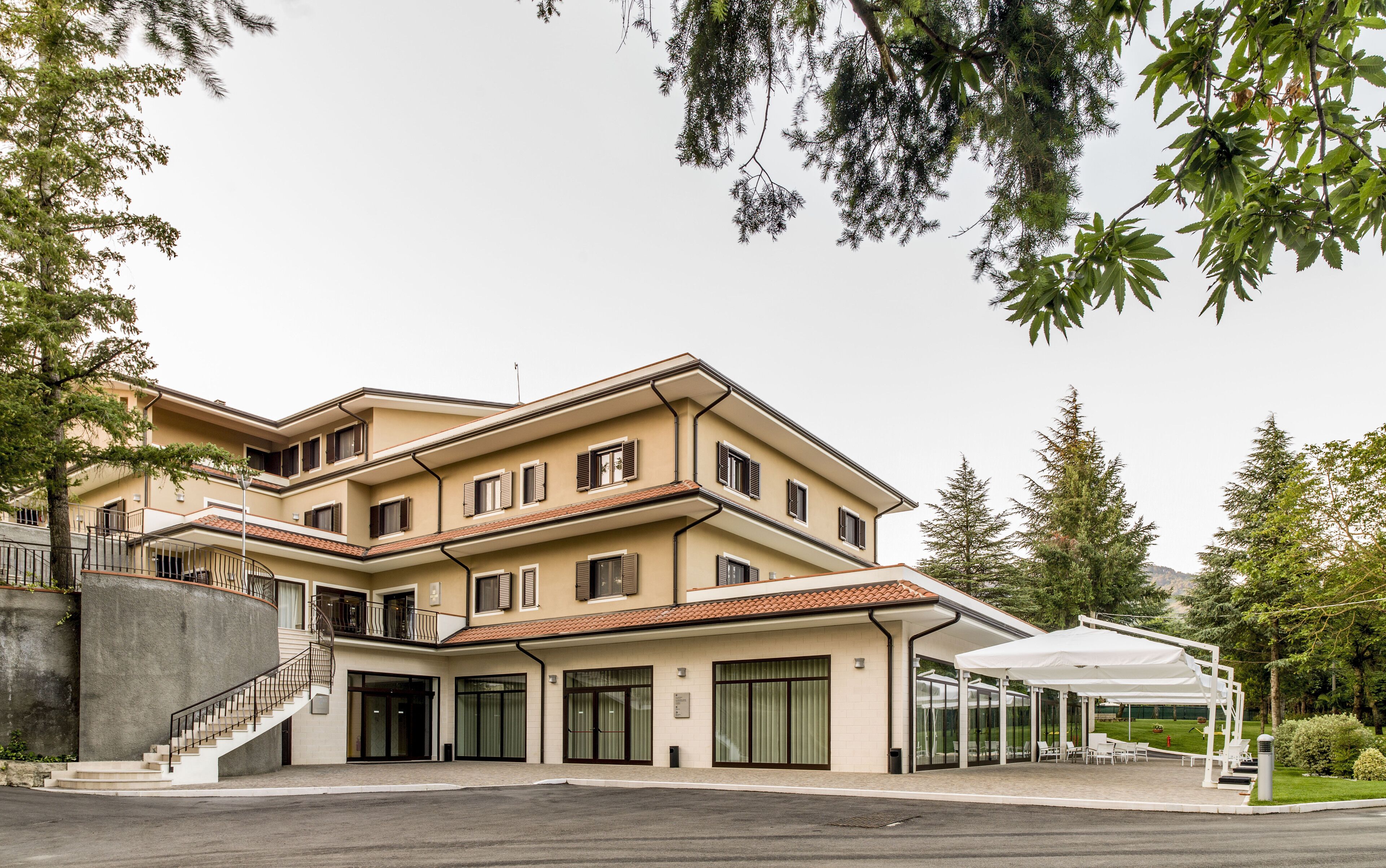 A multi-story hotel with a covered outdoor seating area and a staircase leading to the entrance.