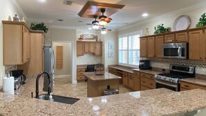 A kitchen with granite countertops, wooden cabinets, a central island, stainless steel appliances, and a ceiling fan. - Spectacular Hot Tub w/ Pool Home on Beautiful Golf Course View,BBQ, & WiFi! (The Villages)