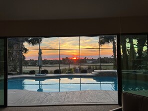 Una piscina con vista su un tramonto attraverso ampie finestre.
