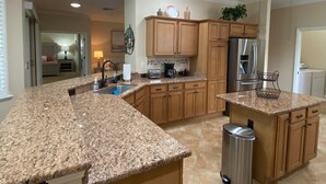 A kitchen with granite countertops, wooden cabinets, a stainless steel refrigerator, and a ceiling fan. - Spectacular Hot Tub w/ Pool Home on Beautiful Golf Course View,BBQ, & WiFi! (The Villages)
