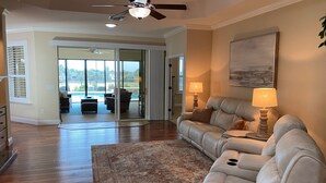 A spacious living room with a large sectional sofa, a ceiling fan, and a view of a pool through glass doors. - Spectacular Hot Tub w/ Pool Home on Beautiful Golf Course View,BBQ, & WiFi! (The Villages)