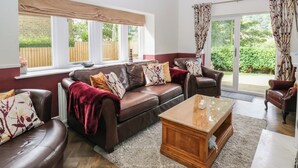 A living room with a brown leather sofa set, a wooden coffee table, and a view of a garden through large windows.