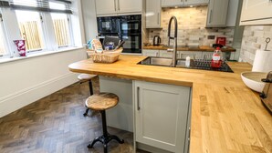 A modern kitchen with a wooden countertop, stainless steel appliances, and a herringbone wood floor.