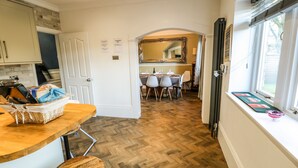 A kitchen with a wooden herringbone floor, a dining area with a table and chairs, and a window with a view of the outdoors.
