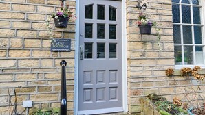 A stone building with a grey door, a sign reading "The Porthole," and hanging flower pots.