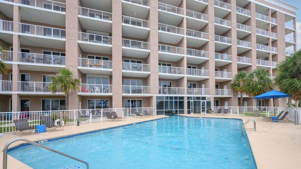 A multi-story hotel with a swimming pool, sun loungers, and a fenced deck area. - 1BR Fort Morgan Condo | Gulf Views + Pool (GULF SHORES)