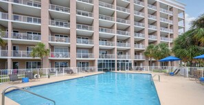 Un hotel de varios pisos con piscina, mobiliario exterior y balcones.