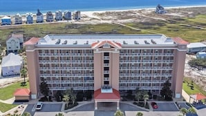 A large hotel with multiple floors, a central courtyard, and a view of the beach and ocean. - 1BR Fort Morgan Condo | Gulf Views + Pool (GULF SHORES)