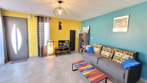 Una sala de estar con un sofá, cojines coloridos, un televisor, una estantería y un banco estampado.