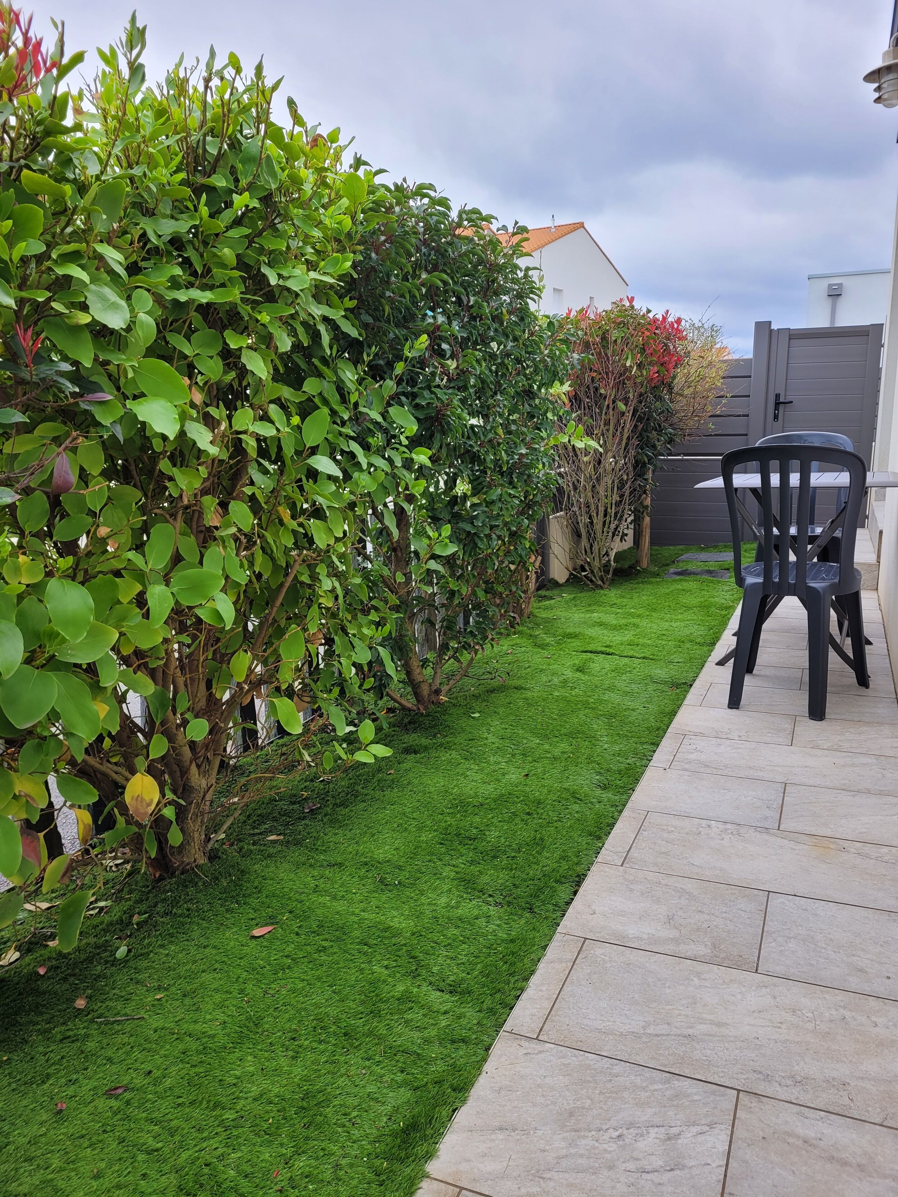 A well-maintained garden with a paved walkway, a chair, and a fence in the background.
